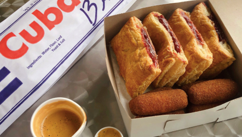 A box of pastries and croquettes with coffee on the side, featuring a Cuban bakery logo in the background.