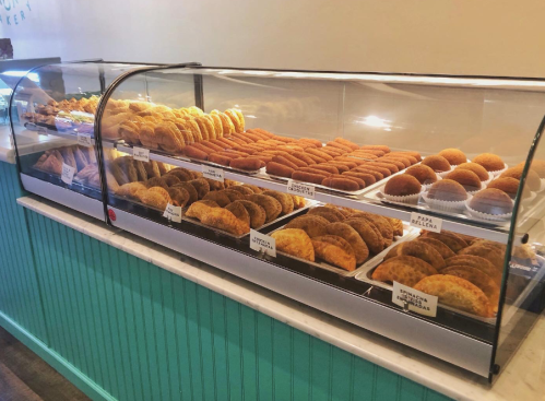 A display case filled with various baked goods, including pastries and cookies, in a colorful bakery setting.