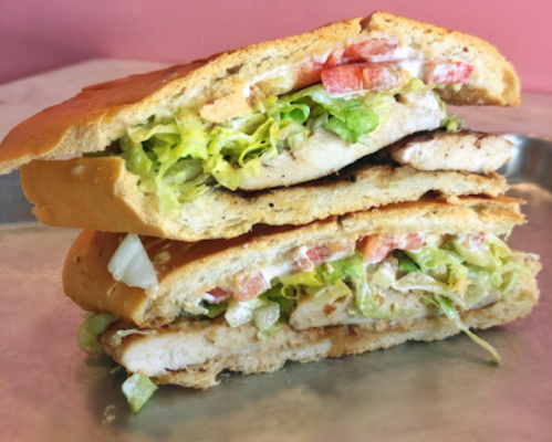 A stacked sandwich with grilled chicken, lettuce, tomatoes, and sauce, served on a toasted bun.