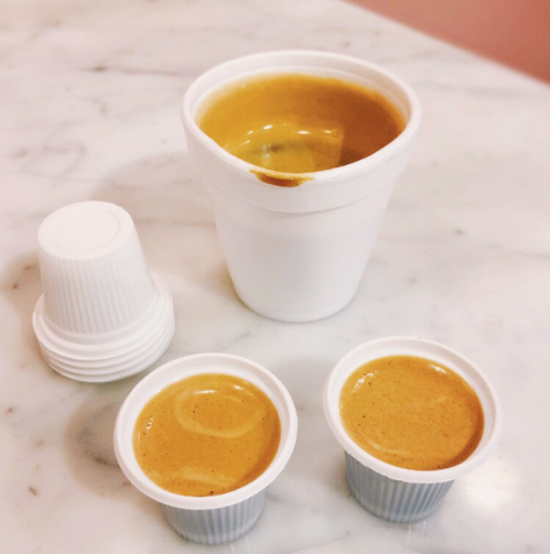 Three white cups on a marble surface: one large cup filled with brown liquid and two smaller cups beside it, also filled.