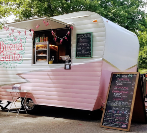 A pink and white food truck with a menu board, serving Cuban cuisine in a park setting.