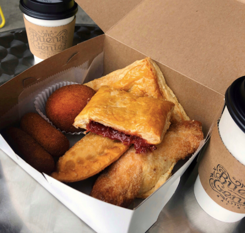 A takeout box filled with pastries and snacks, alongside two coffee cups.