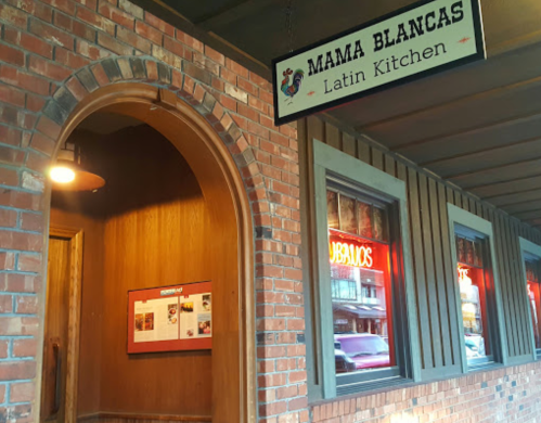 Sign for "Mama Blancas Latin Kitchen" above an entrance with warm wooden tones and illuminated menu display.