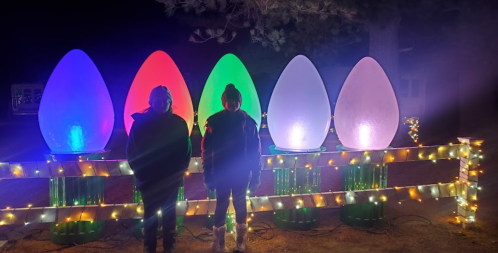 Two people stand in front of large, illuminated egg-shaped decorations, surrounded by festive lights at night.