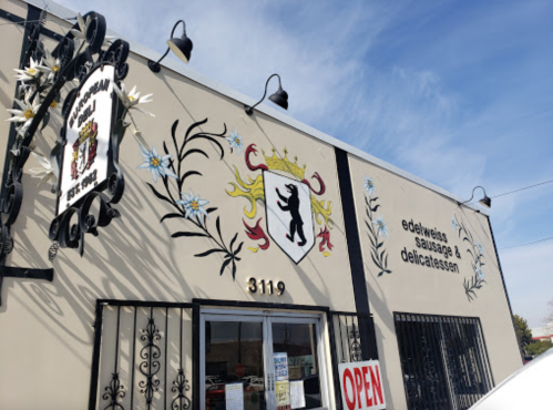 A storefront with decorative murals, featuring a coat of arms and signs for "Edelweiss Sausage & Delicatessen."