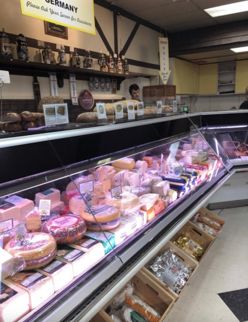 A display case filled with various cheeses and snacks in a shop, with a staff member in the background.