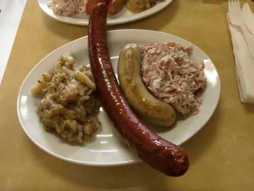 A plate with three types of sausage and a serving of shredded meat, accompanied by a side of potato dish.