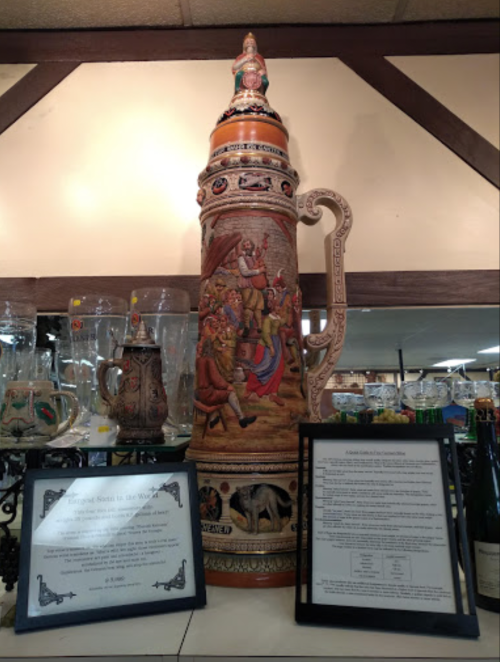 A large decorative beer stein with intricate carvings, displayed alongside informational plaques in a shop.