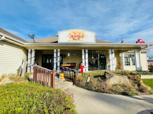 A charming Amish-themed building with a sign, surrounded by greenery and a clear blue sky.
