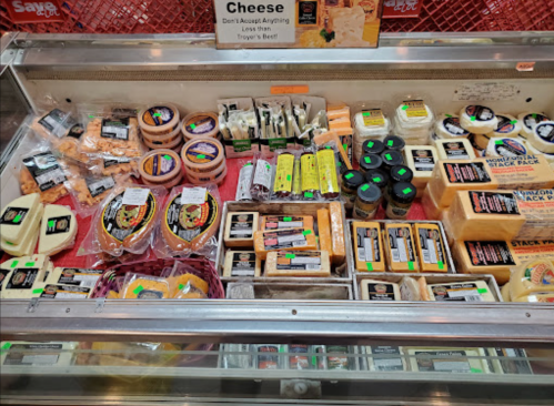 A display case filled with various types of cheese, labeled and organized in a grocery store.
