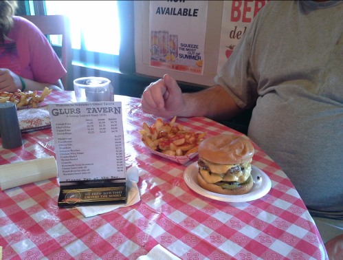 A table with a menu, a plate of fries, and a cheeseburger in a casual dining setting.