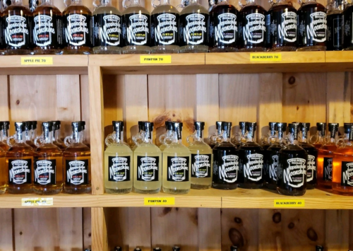 Shelves filled with various bottles of flavored spirits, labeled with names like "Apple Pie" and "Blackberry."