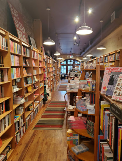 A cozy bookstore aisle lined with wooden shelves filled with books and colorful displays, featuring a warm, inviting atmosphere.