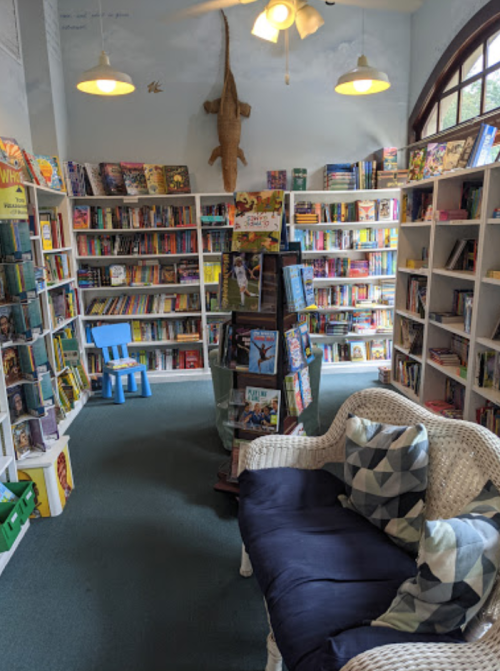 Cozy library interior with bookshelves, a blue chair, and a decorative alligator hanging from the ceiling.