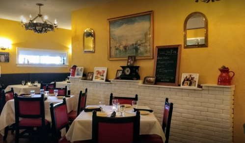 Cozy restaurant interior with yellow walls, red chairs, and a decorative fireplace featuring framed photos and a chalkboard.