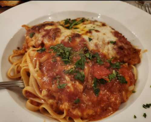 A plate of pasta topped with marinara sauce, melted cheese, and fresh herbs, served with a fork on the side.