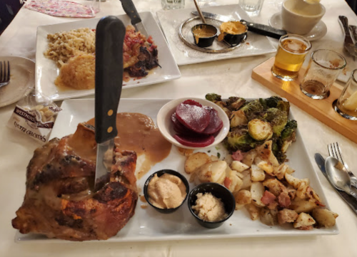 A plate with a large pork chop, gravy, roasted potatoes, beets, and Brussels sprouts, with small cups of sauce on the side.