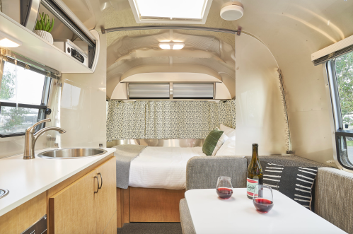 Cozy interior of a modern camper, featuring a kitchenette, dining area, and a bed with soft lighting and decor.