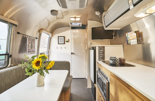 Interior of a modern Airstream trailer featuring a dining area, kitchenette, and bright sunflowers on the table.