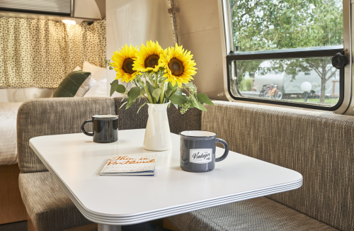 A cozy interior of a camper with a table, two mugs, and a vase of sunflowers by a window.