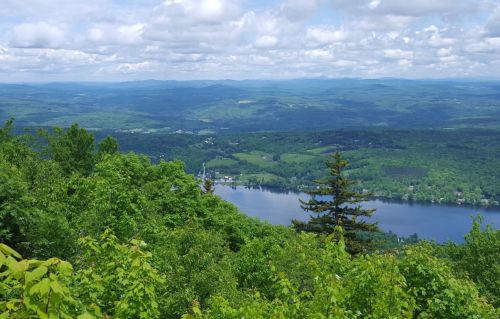 A panoramic view of lush green hills and a river under a cloudy sky, showcasing nature's beauty.