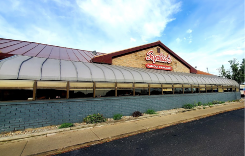 Exterior of Sophie's Famous Pancakes restaurant with a curved glass awning and a brick facade under a blue sky.