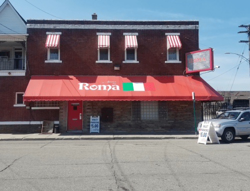A red-brick building with a red awning labeled "Roma," featuring Italian flags and a sign advertising food specials.