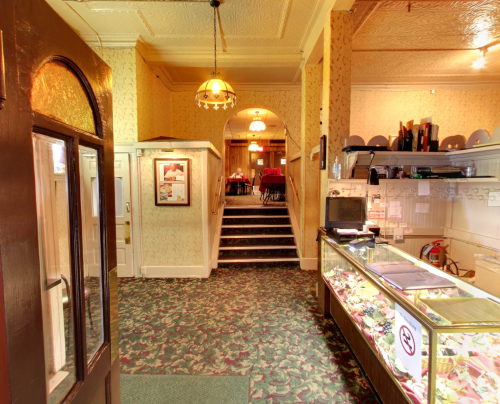 Interior view of a restaurant entrance, featuring a display case and stairs leading to a dining area with tables.