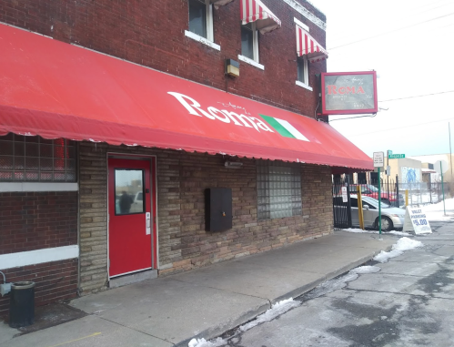 Exterior of a restaurant named "Roma," featuring a red awning and a red door, with snow on the ground.