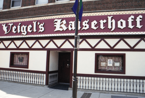 Exterior of Veigel's Kaiserhoff, a restaurant with a red and white sign, featuring decorative trim and a welcoming entrance.