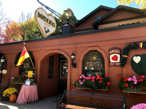 A charming restaurant with a red exterior, flower boxes, and a German flag, surrounded by autumn foliage.