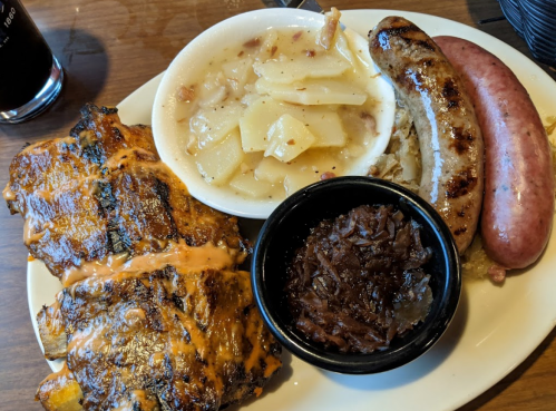 A plate featuring grilled ribs, sausages, sauerkraut, and a side of potato dish.