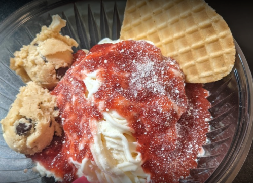 A bowl of ice cream topped with strawberry sauce, whipped cream, cookie dough, and a waffle cone.