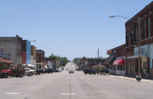 A quiet street in a small town, lined with shops and parked cars under a clear blue sky.