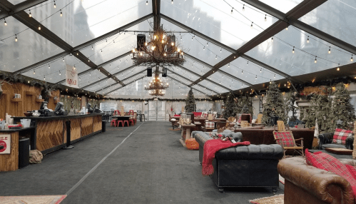 A cozy, decorated tent with string lights, seating areas, and Christmas trees, creating a festive atmosphere.