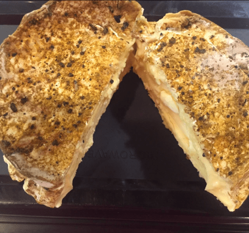 A sliced sandwich with a golden-brown crust, revealing melted cheese and spices inside.