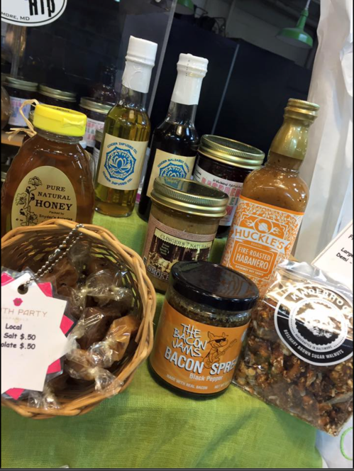 A display of various local food products, including honey, oils, sauces, and snacks, arranged on a green tablecloth.