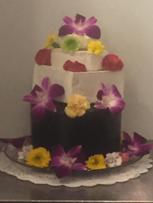 A three-tiered cake decorated with colorful flowers and a lace doily at the base.