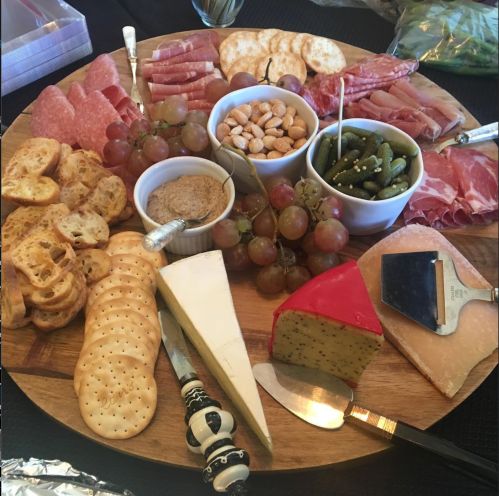 A wooden platter filled with assorted meats, cheeses, crackers, nuts, and grapes, arranged for a charcuterie board.