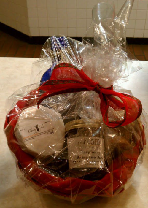 A gift basket wrapped in cellophane, featuring various items and a red ribbon on top.