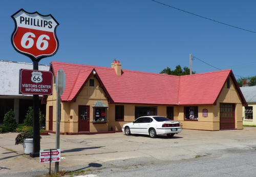 Historic Phillips 66 building with a red roof and sign, serving as a visitors center, set in a small town.