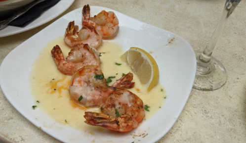 A plate of grilled shrimp in a buttery sauce, garnished with parsley and a lemon wedge.