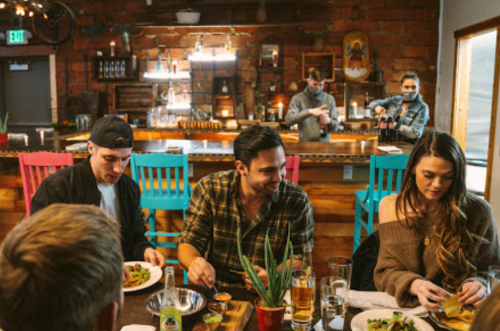 A group of friends enjoying a meal at a cozy restaurant with a bar in the background.