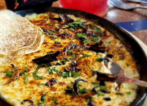 A close-up of a creamy dish topped with herbs and spices, served with flatbread on the side.