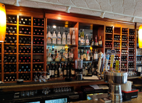 A well-stocked bar featuring shelves of wine bottles and various spirits, with taps and glassware on the counter.
