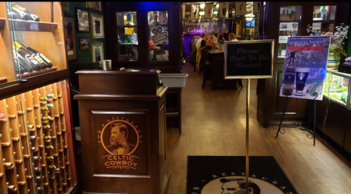Interior of a restaurant with a welcoming sign, wooden decor, and patrons in the background. Celtic Cowboy branding visible.