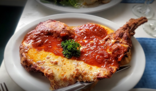A heart-shaped plate of chicken parmesan topped with marinara sauce and melted cheese, garnished with parsley.