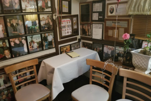 A cozy dining area with a white tablecloth, surrounded by framed photos on the walls and empty wooden chairs.