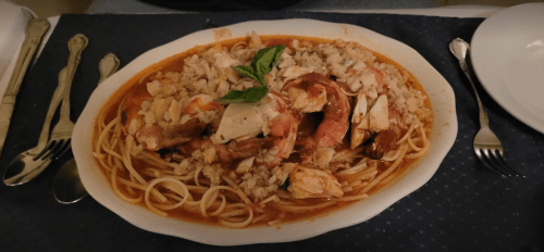 A large platter of pasta topped with shrimp, crab, and rice, garnished with a basil leaf.