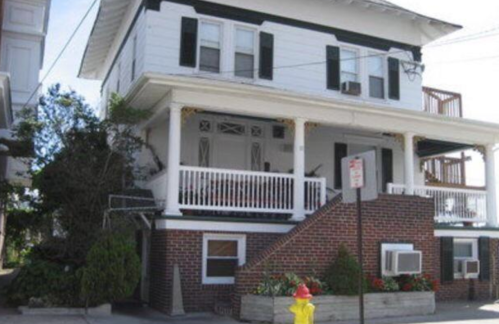 A two-story white house with black shutters, a porch, and a fire hydrant in front.